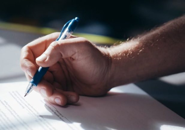 Detailed shot of a hand holding a blue pen while signing a document. Ideal for legal and business themes.