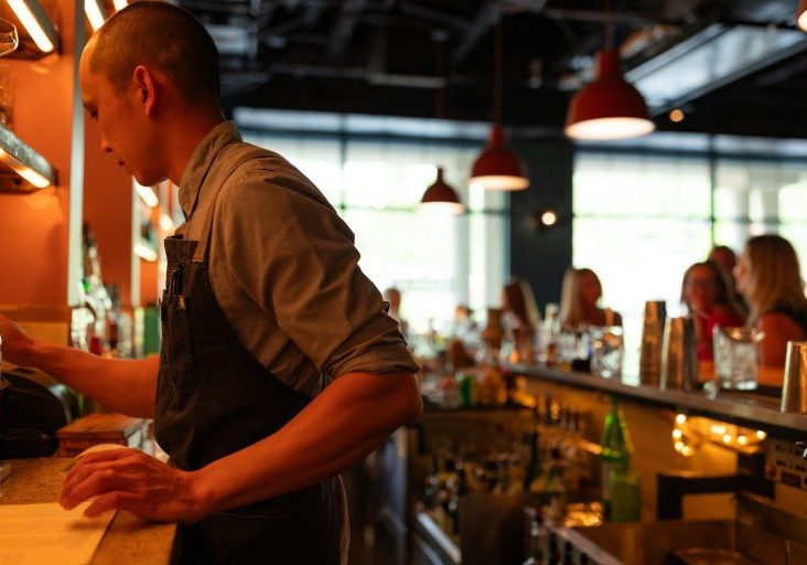 A man standing at a bar with a bottle of wine