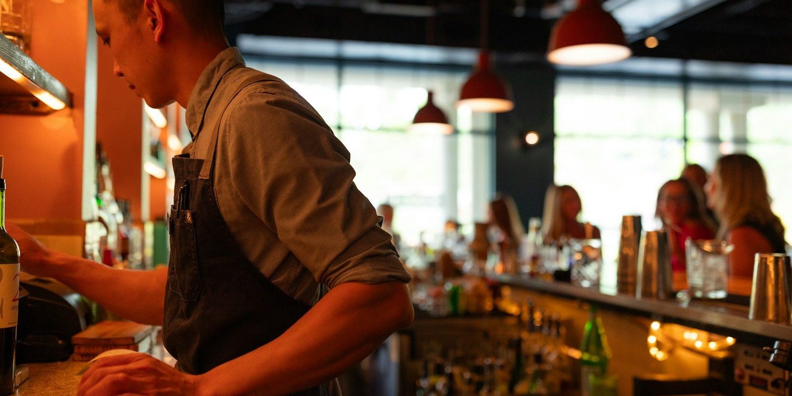 A man standing at a bar with a bottle of wine